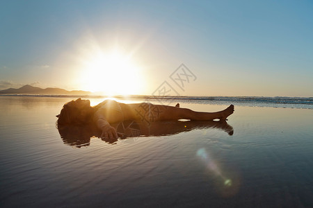 日落时分躺在海滩浅水中的妇女图片
