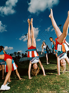 女孩啦啦队员啦啦队员在球场上倒立背景