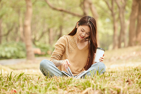 春游季节年轻女性草地上看书喝咖啡背景