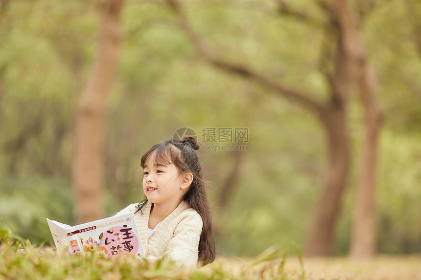 小女孩趴在草地上看童话故事图片