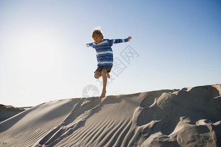 男孩在沙丘上跳跃图片