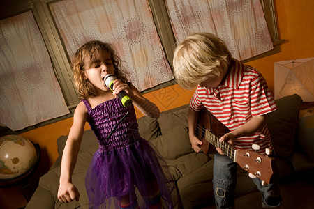 唱歌的孩子女孩用麦克风唱歌，男孩弹吉他背景
