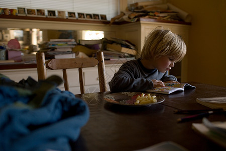 小男孩坐在餐桌旁看书厨房高清图片素材