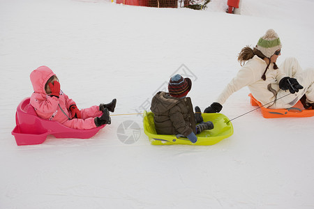 母亲用雪橇拉着两个孩子滑雪高清图片