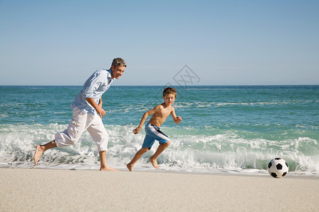海边的孩子父子俩在海边踢足球背景