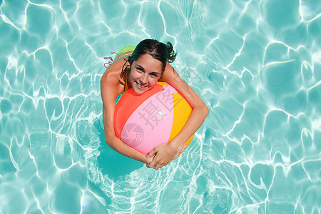 一个沙滩球带沙滩球的在游泳池里的年轻女子背景