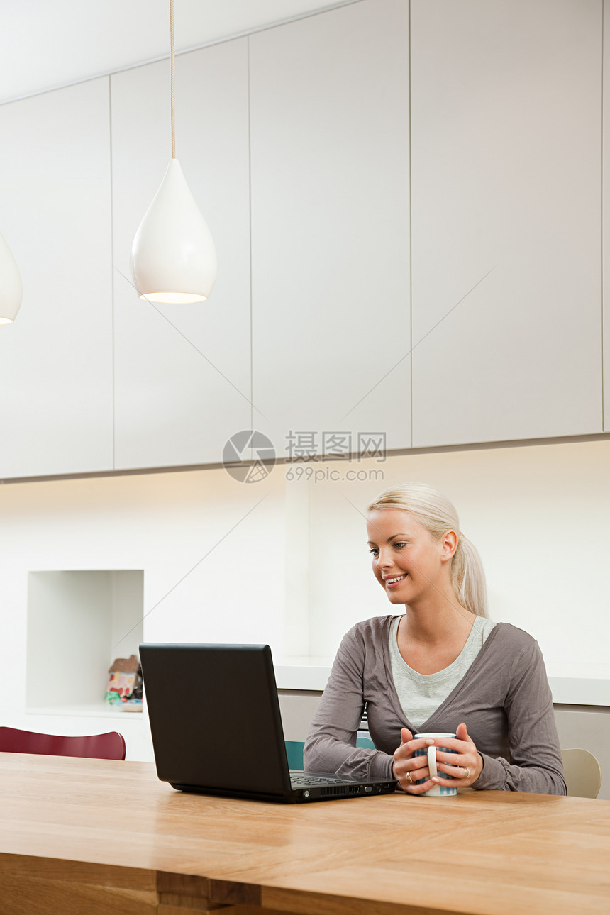 坐在桌旁的年轻女子拿着笔记本电脑图片