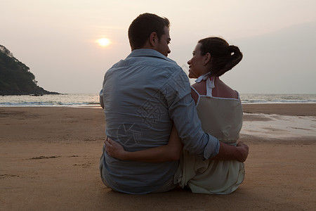 日落时分坐在海滩上的一对夫妇图片