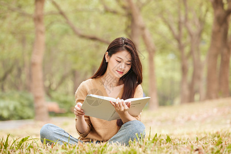 年轻女性坐在草地上看书高清图片