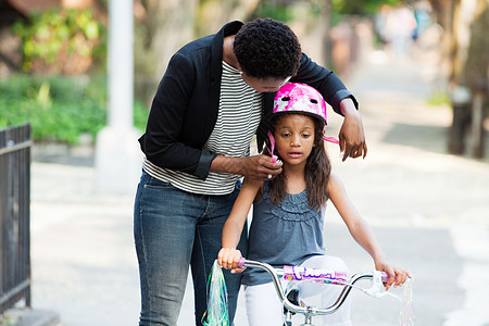 母亲正在调整女儿的自行车头盔图片