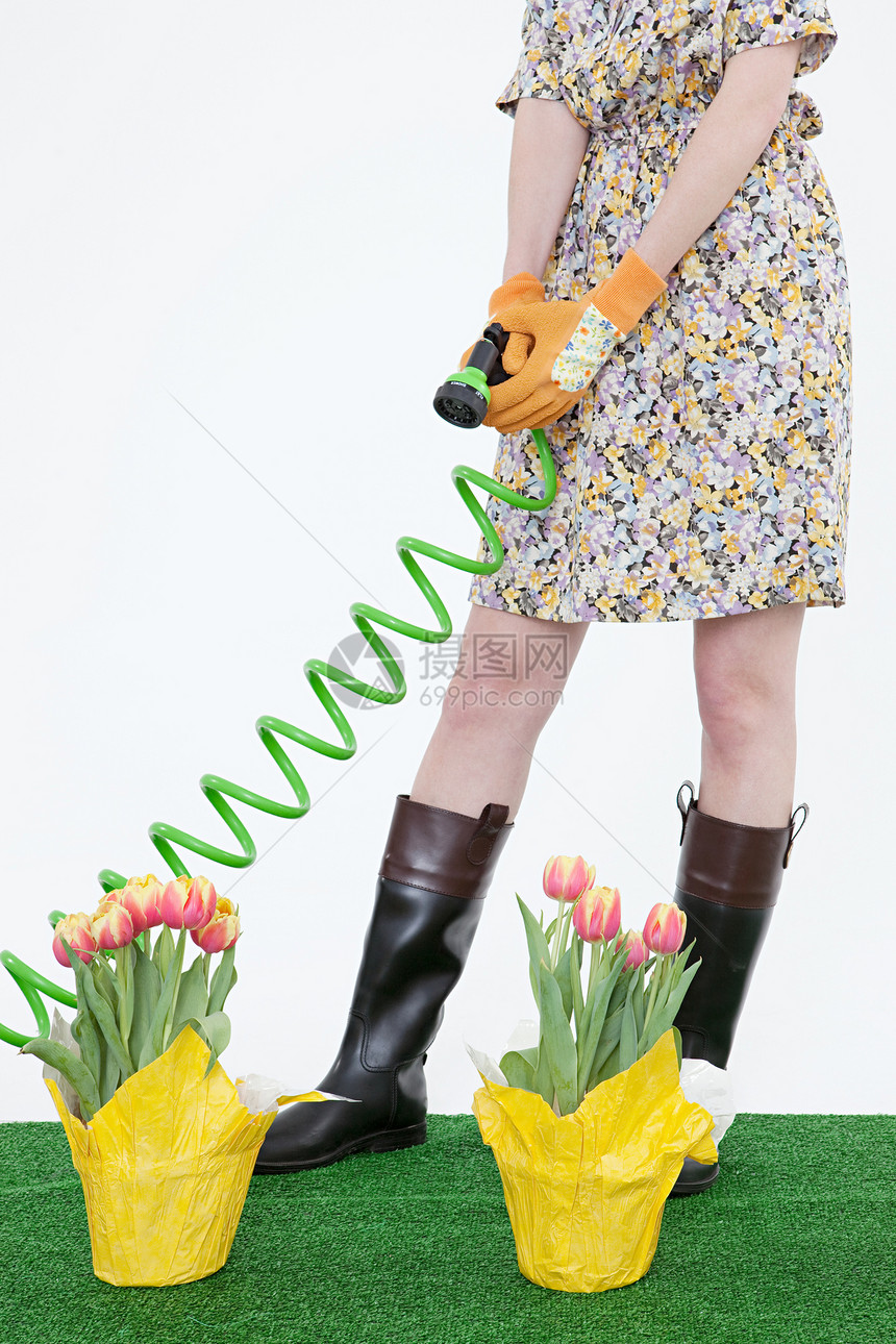 在人造草坪上带着软管和花的女人图片