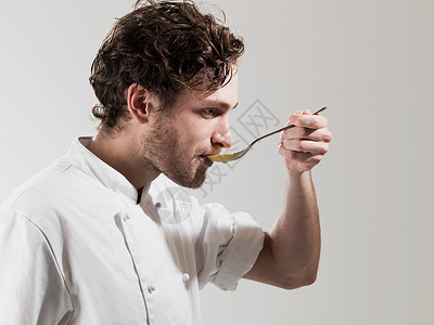 厨师在白色背景下用勺子品尝食物图片