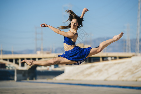 美国加利福尼亚州洛杉矶市一名年轻女子微笑着在半空中做劈叉的侧视镜头背景图片