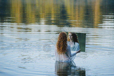 年轻女子站在湖中拿着镜子看着镜子里的倒影图片