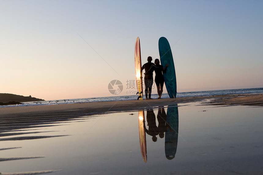 一对夫妇拿着冲浪板站在海滩上图片
