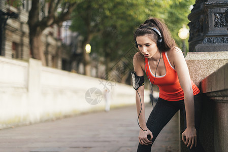 女跑步者戴着耳机在河边休息高清图片