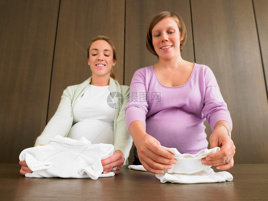 叠婴儿服装的孕妇图片