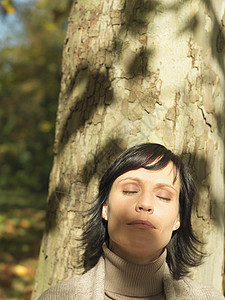 阳光下靠在树上的女人图片