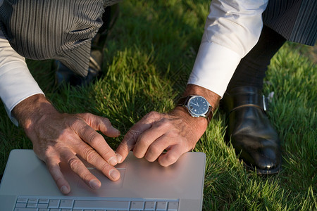 蹲在草地上使用笔记本电脑的男人图片