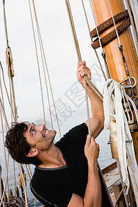 在桅杆上坐在帆船甲板上拉绳的男人背景