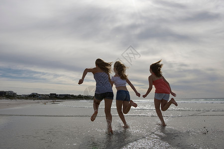 三个十几岁的女孩在海滩上跑步图片