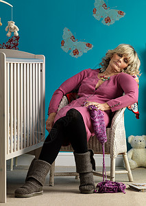 熟女睡在婴儿床旁边的椅子上背景图片
