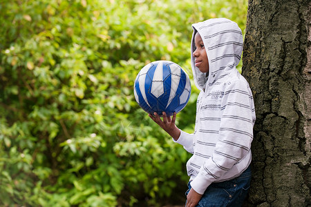 足球衫男孩抱着球靠在树上背景