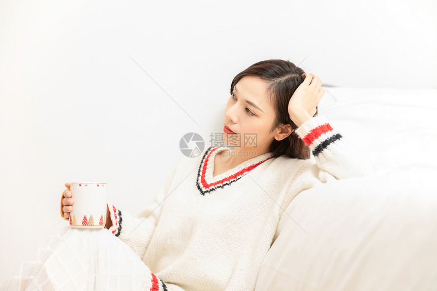 冬季青年女性床边拿着杯子思考图片