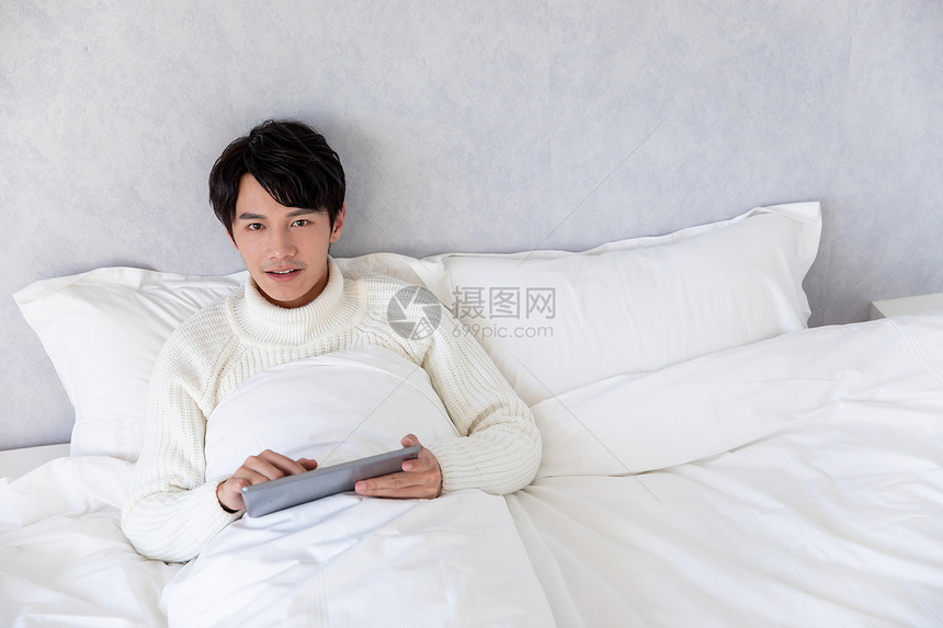 青年男性躺在床上使用平板电脑图片