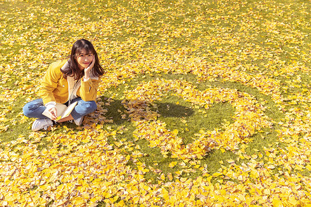 黄色爱心对话框坐在铺满银杏叶的草坪上看书的女孩背景