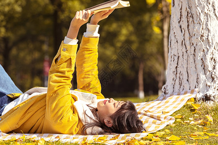 躺在铺满银杏叶的毯子上看书的女孩高清图片