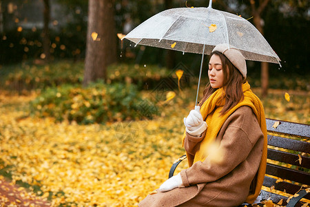 秋季银杏树下悲伤美女撑伞背景图片