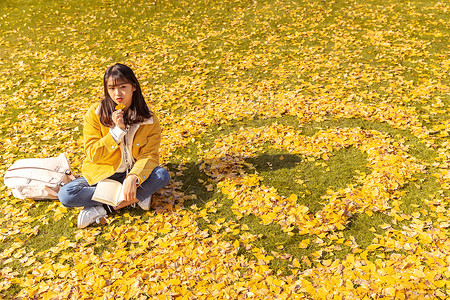 坐在铺满银杏叶的草坪上的女孩 图片