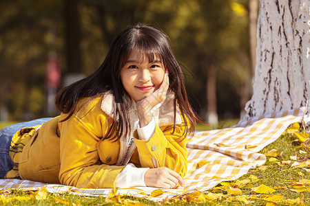 甜美女孩趴在铺满银杏叶的毯子上高清图片