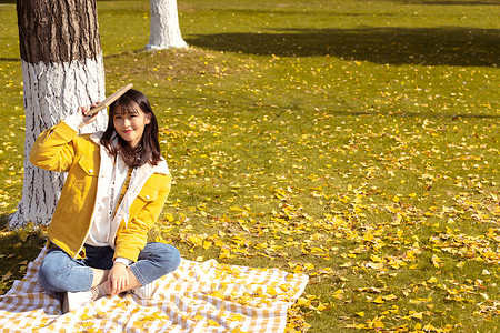 坐在铺满银杏叶的毯子上手拿书本的女孩高清图片