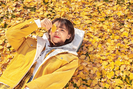 躺在铺满银杏叶草坪上的甜美女孩高清图片
