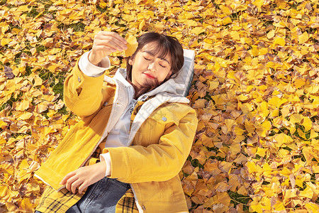 躺在铺满银杏叶草坪上的甜美女孩背景图片