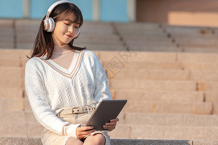 戴耳机听音乐的美女甜美大学生户外听音乐背景