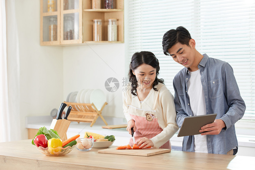 年轻夫妻拿着平板电脑学习做菜图片