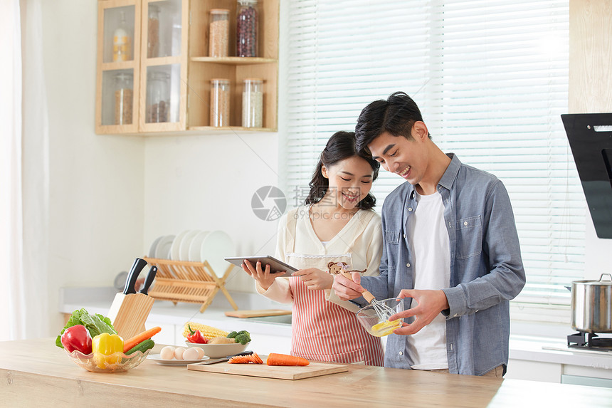 年轻夫妻拿着平板电脑学习做菜图片