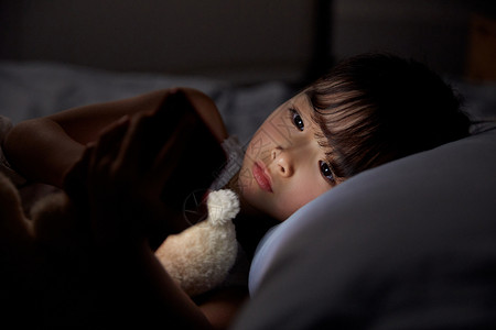 作息安排小女孩夜晚躺床上玩手机背景