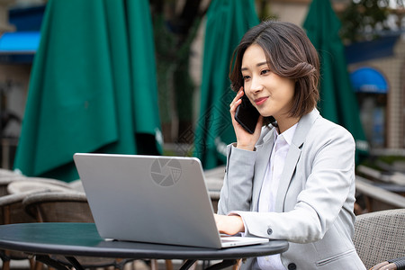 商务职业女性在户外看着笔记本电脑打电话图片