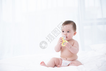 含在嘴里婴儿在床上拿着玩具玩耍背景