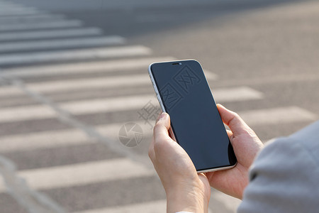 拿手机的人女性拿手机过人行横道局部特写背景
