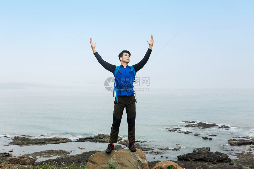 野外海边石头上的男性举起双臂图片