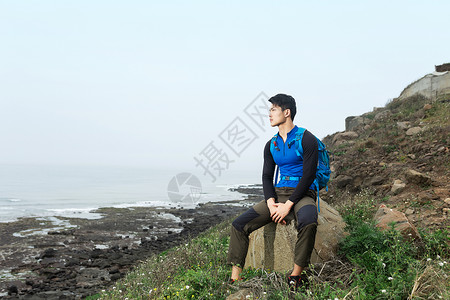 背包坐海边石头上的男性图片