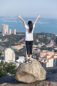 登山欢呼厦门城市公园山顶站石头上举起双臂欢呼的美女背景