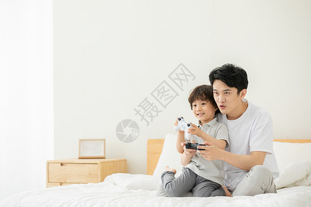 爸爸抱着儿子在床上打电子游戏图片