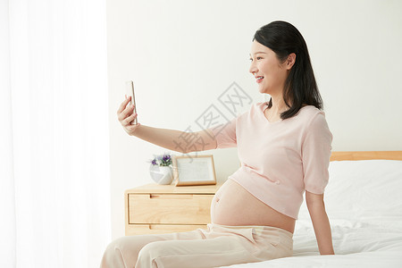 孕妇坐床上玩手机图片