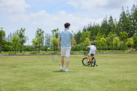 爸爸陪伴小男孩骑自行车背影高清图片
